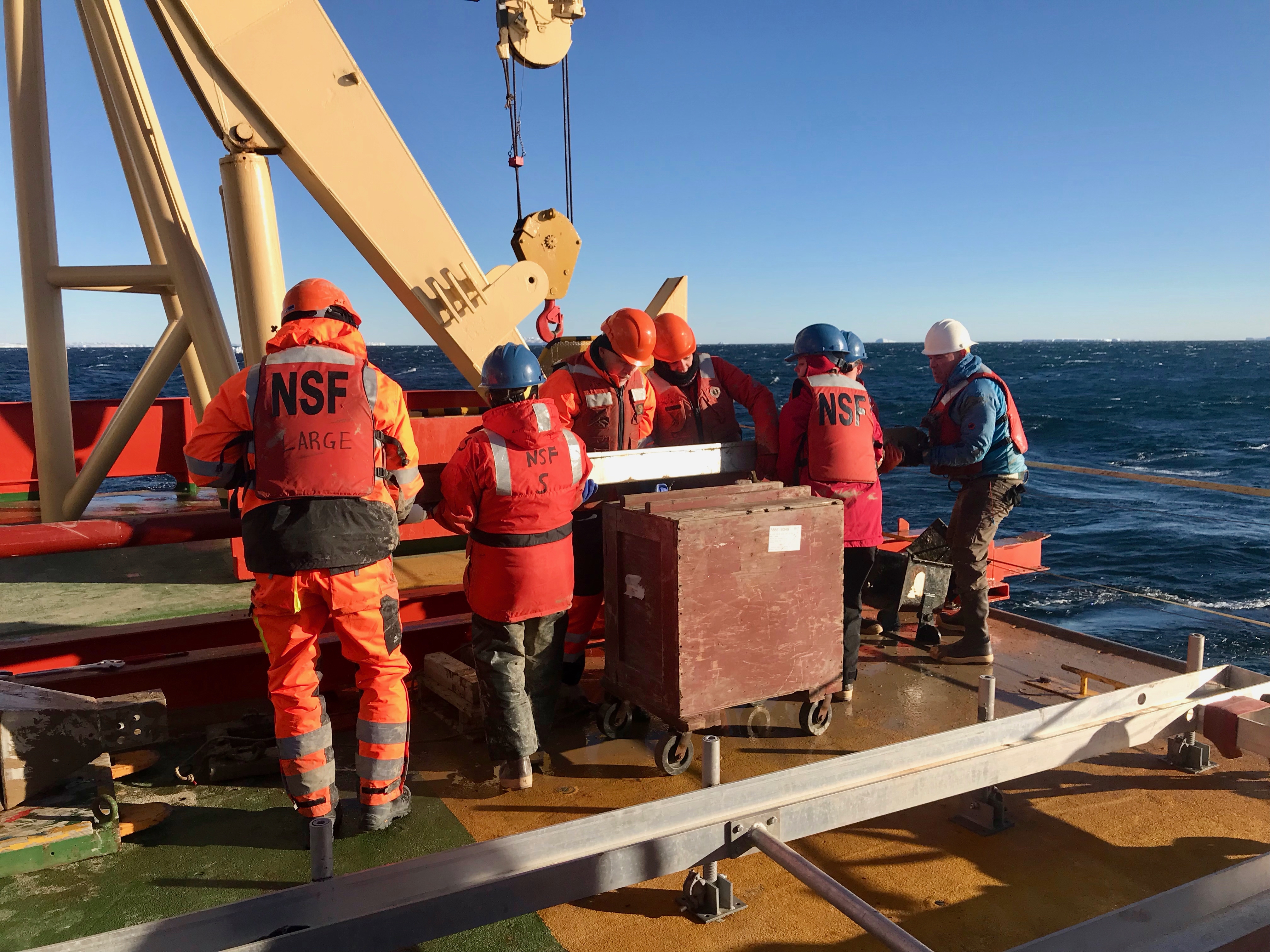 The THOR team lifts the Kasten core from the deck onto the trolley to bring it inside the ship where it will be completely opened and the sediments sampled (from left to right: James Kirkham, Victoria Fitzgerald, Rob Larter, Kelly Hogan, Rachel Clark, Becky Minzoni, and Jack Greenberg).